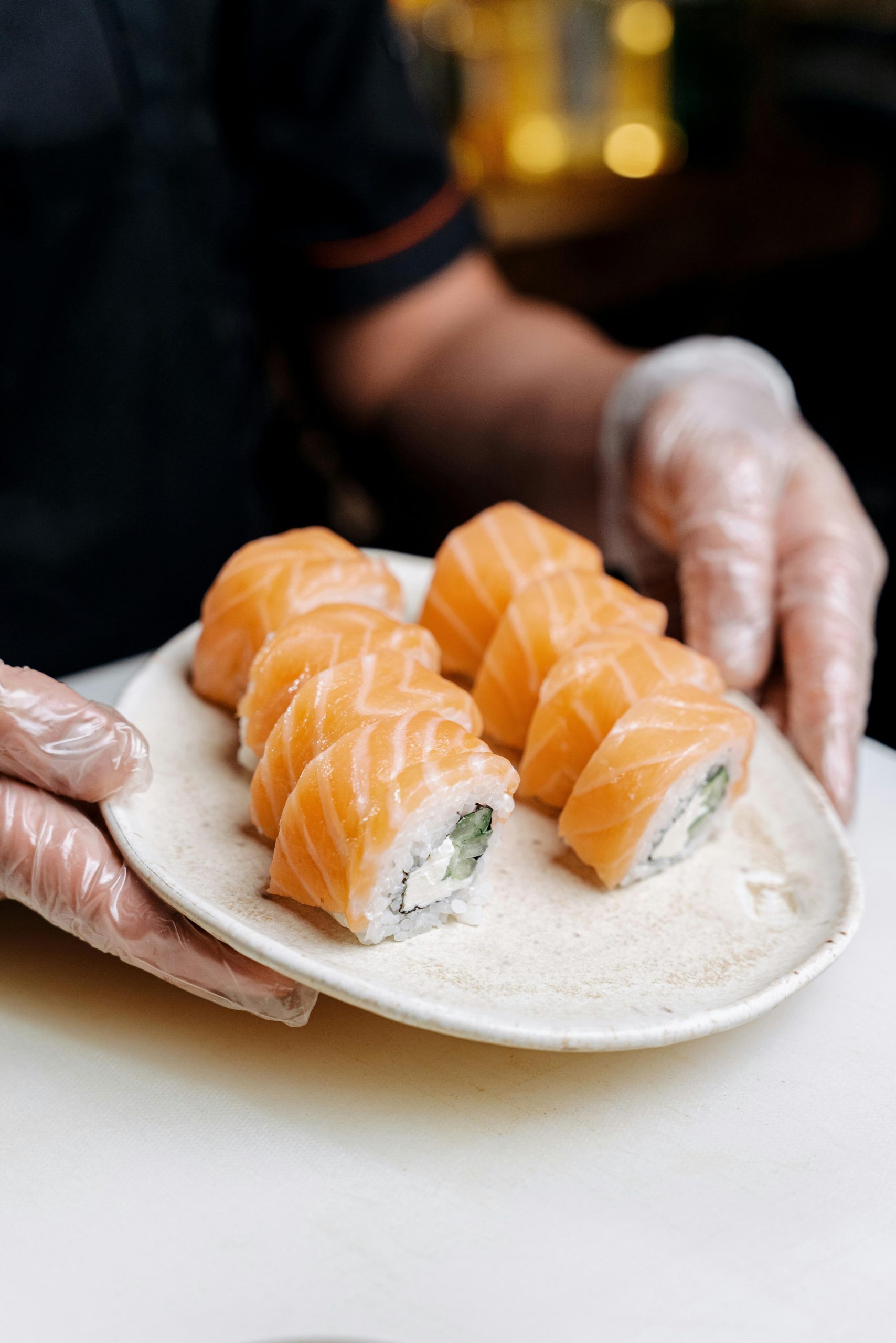 Fresh salmon cream‑cheese sushi rolls held by gloved hands at Otoro Sushi & Ramen, a Sushi Restaurant in Omaha